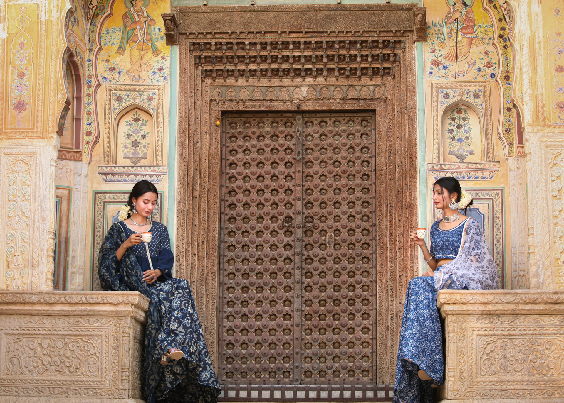two women sitting on a wall looking at their cell phones